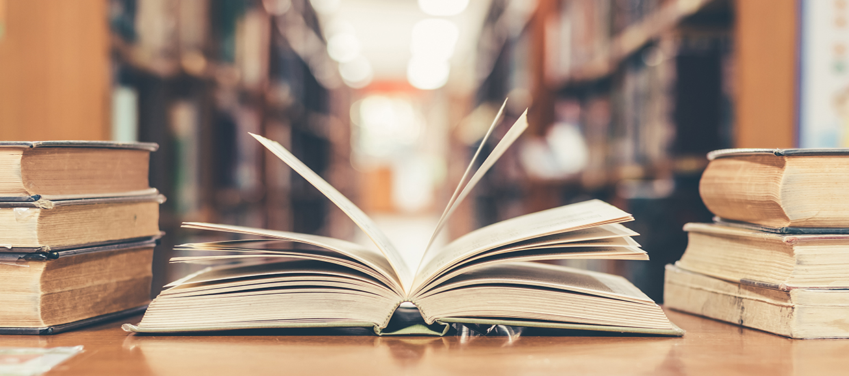 A stock photo of an open book next to two stacks of books.